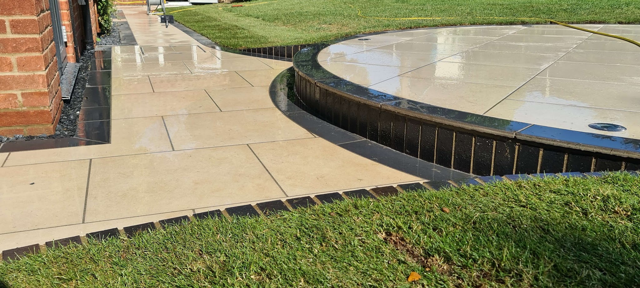 Curved raised porcelain terrace with dark edging beside a lawn