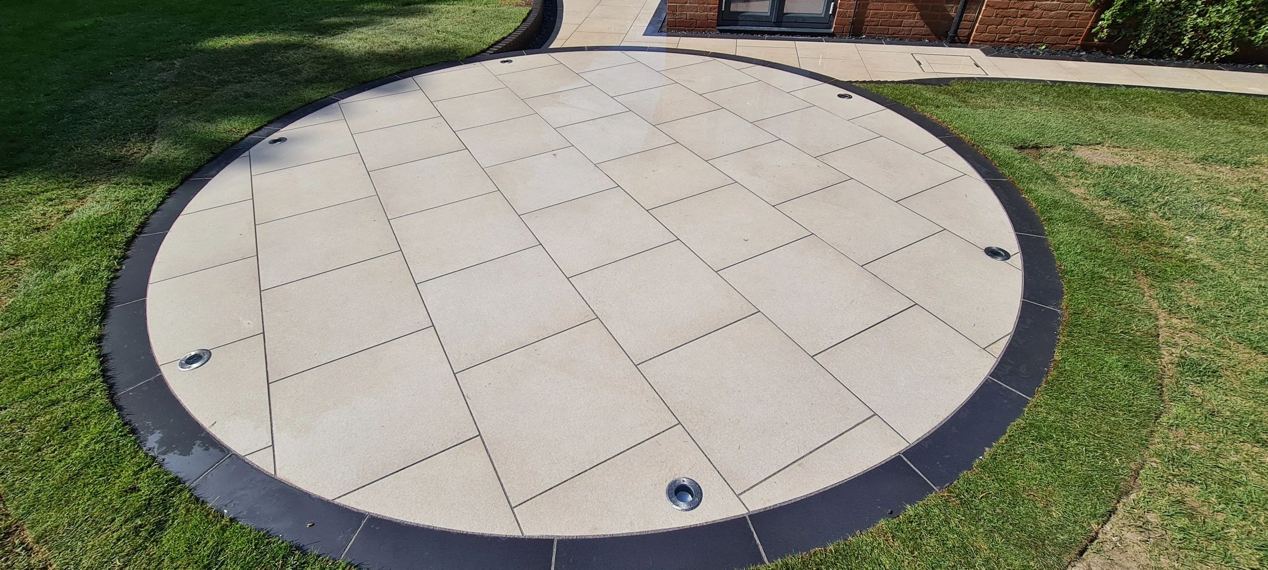 Circular porcelain patio with uplighters set into a lawn